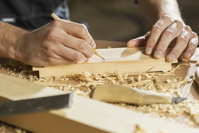 Mans marcant amb un llapis una peça de fusta al taller